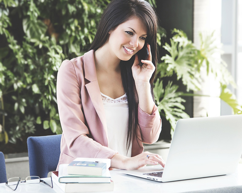 Woman talking on a mobile phone while browsing the internet on her laptop